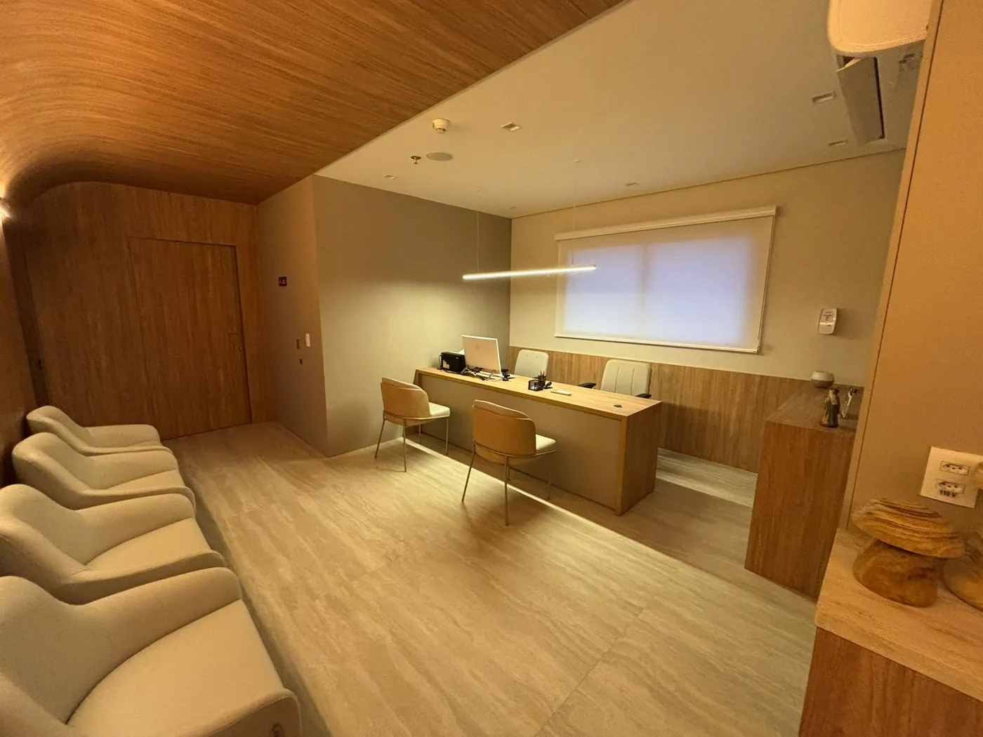 Sala de atendimento da Clínica Allmare, com mesa, poltronas claras e paredes de madeira